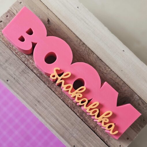 3D-gedruckter Schriftzug Boom Shakalaka in Pink und Orange auf Holzblock – DIY-Deko aus STL- und 3MF-Datei von The Vectorians