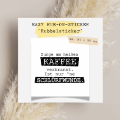 Rub-On Rubbelsticker mit Kaffee-Spruch „Zunge am heißen Kaffee verbrannt. Ist nur ’ne Schlürfwunde.“ im Format 85 × 55 mm, platziert auf weißem Hintergrund
